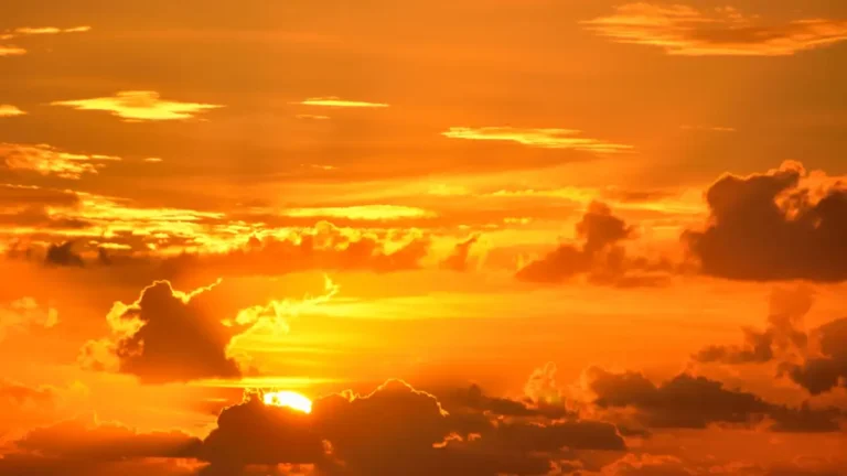 Golden-orange sunset with dark clouds partially obscuring the sun.