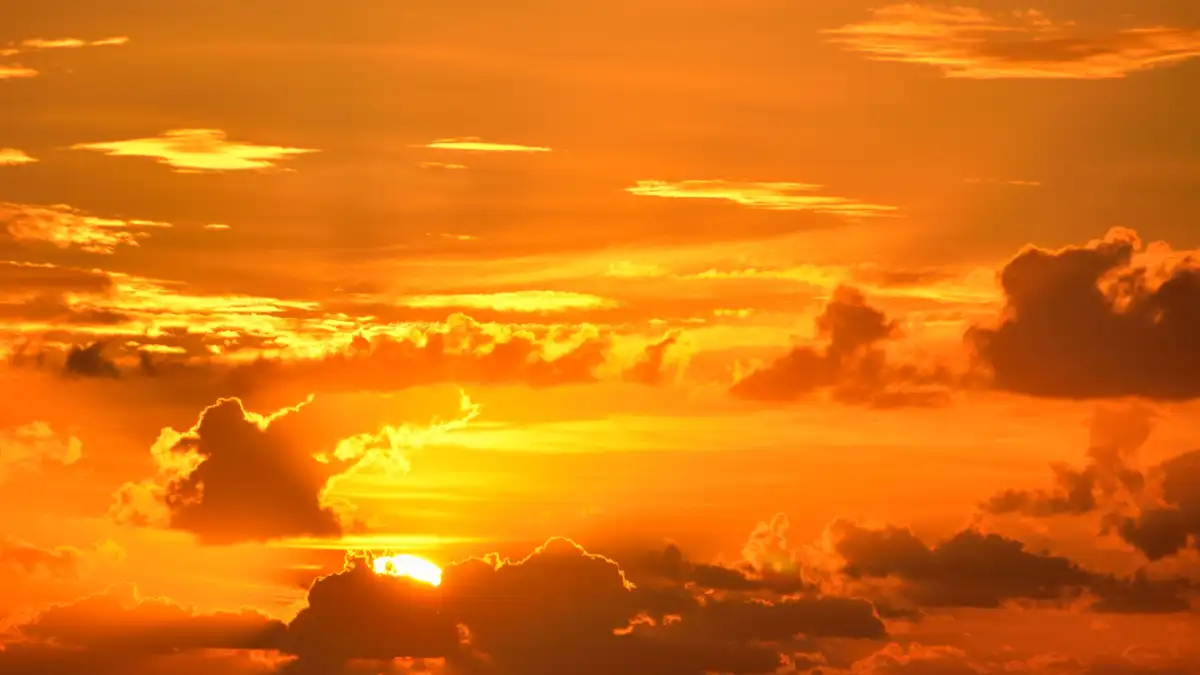 Golden-orange sunset with dark clouds partially obscuring the sun.