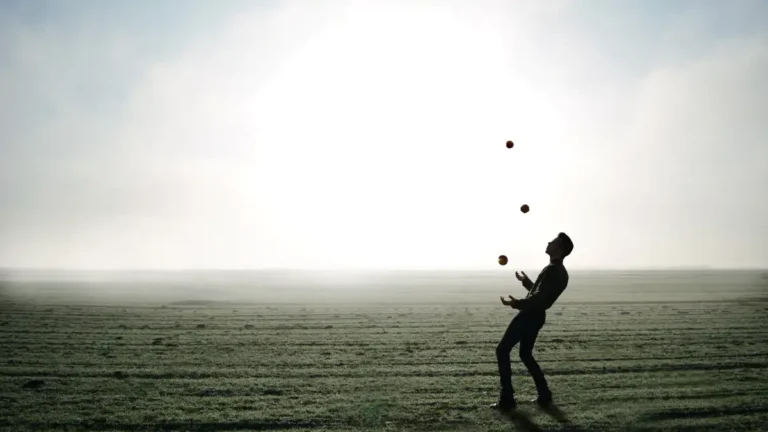 Silhouette of a person juggling four balls in an open field at sunrise.