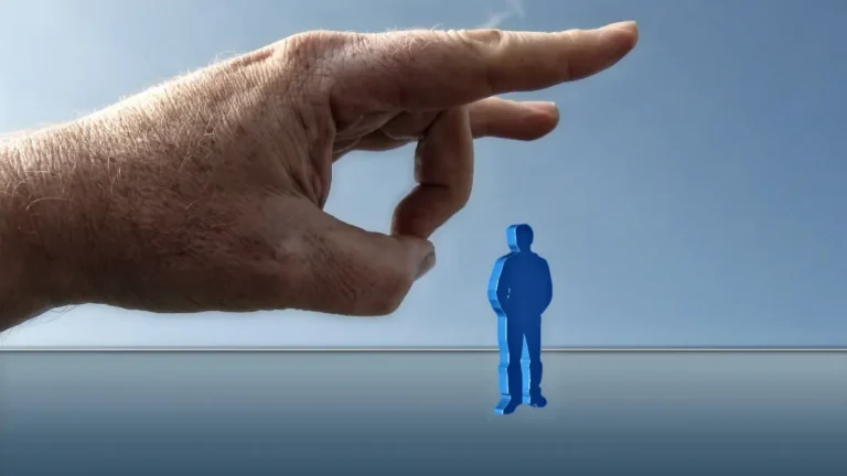 A large human hand flicks away a small blue figure of a person under a clear sky.