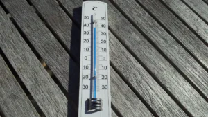 A thermometer lying on a wooden table in direct sunlight, showing an artificially high temperature reading.