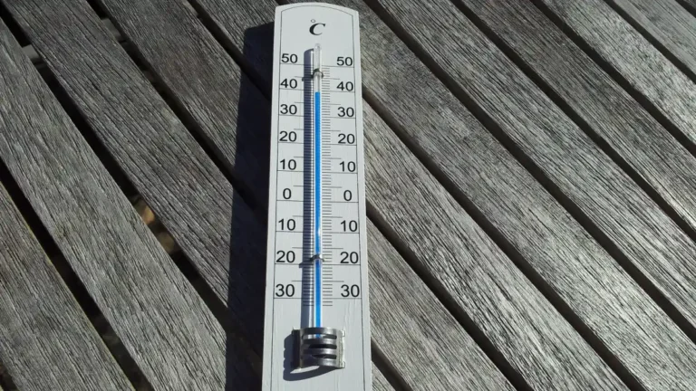A thermometer lying on a wooden table in direct sunlight, showing an artificially high temperature reading.