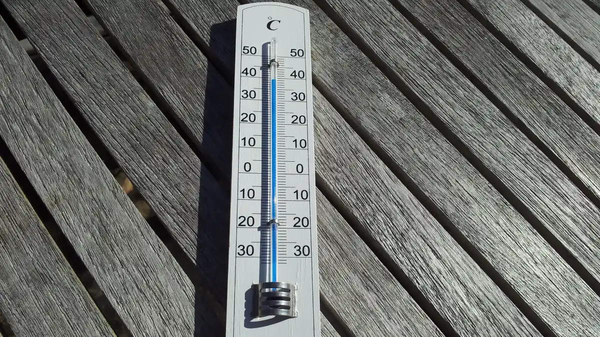 A thermometer lying on a wooden table in direct sunlight, showing an artificially high temperature reading.