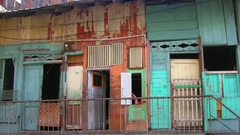 Row of weathered wooden houses with peeling paint in faded turquoise, red, and cream tones.
