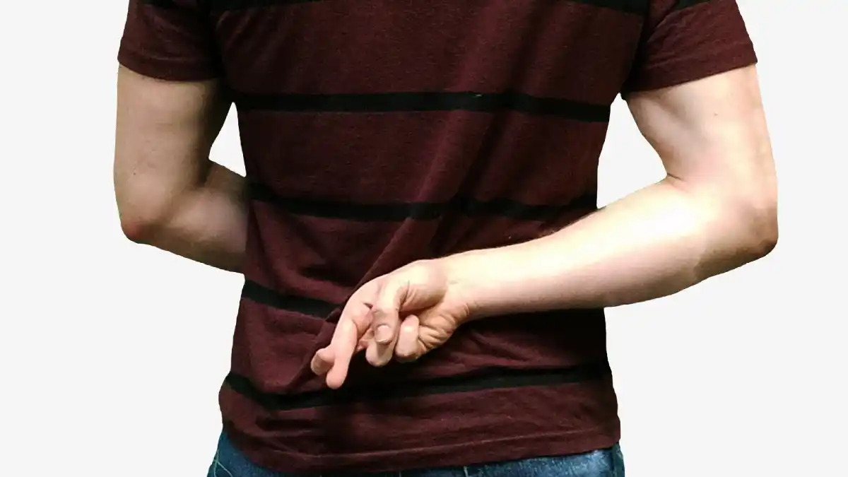 A person standing with one hand behind their back, fingers crossed — symbolizing a hidden lie or broken promise.