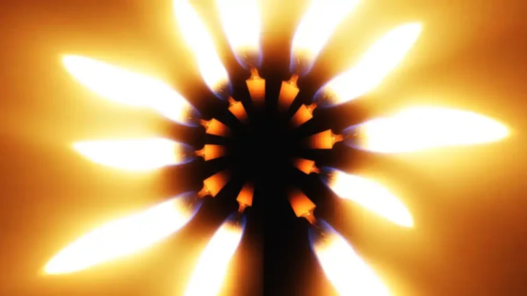 Close-up of a glowing gas burner with bright flames radiating outward against a warm orange background.