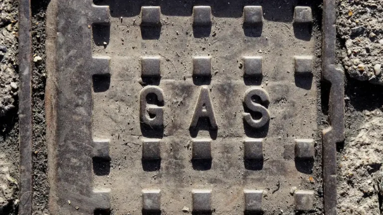 Close-up of a weathered cast-iron gas utility cover embedded in rough concrete, marked “GAS”