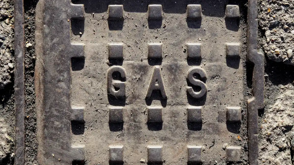Close-up of a weathered cast-iron gas utility cover embedded in rough concrete, marked “GAS”