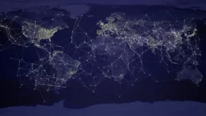 A world map at night showing illuminated cities connected by a glowing web of lines, symbolizing the global network of trade, communication, and power.