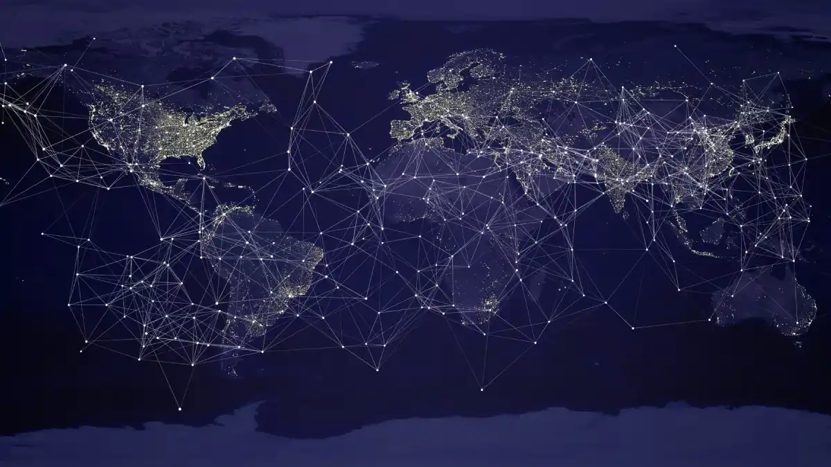 A world map at night showing illuminated cities connected by a glowing web of lines, symbolizing the global network of trade, communication, and power.