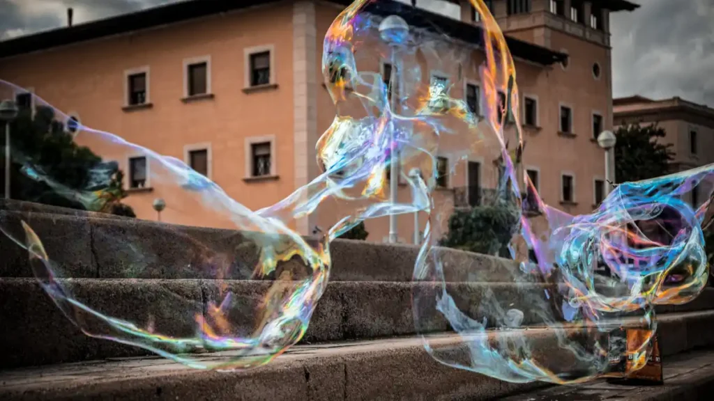 Giant iridescent soap bubbles drifting across weathered stone steps in front of a faded building.