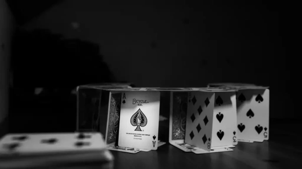 A fragile house of cards in black and white, spotlighted to reveal its precarious construction.