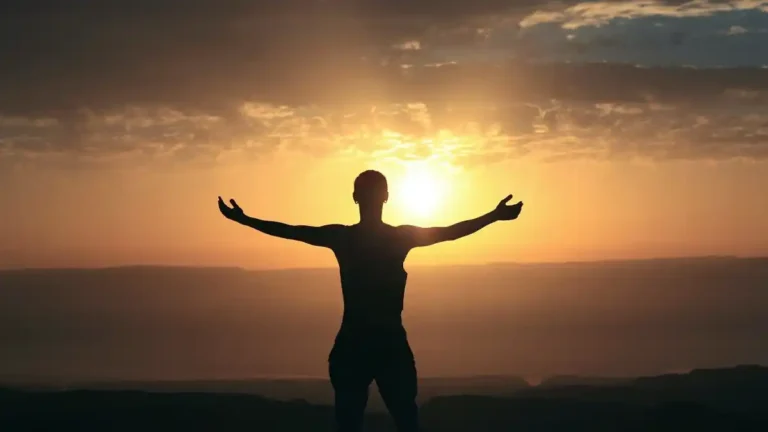 Silhouette of a person with arms outstretched at sunrise over a vast horizon, symbolizing solitude and freedom.
