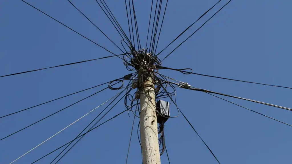Utility pole with a chaotic tangle of wires spreading in all directions against a clear blue sky.