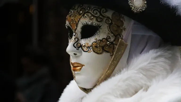 Ornate white Venetian carnival mask with gold detailing and feathers, symbolizing the hidden identities and polite illusions behind social and institutional roles.