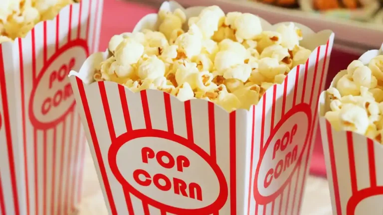 Close-up of striped popcorn containers filled with popcorn at a cinema snack stand, symbolizing entertainment culture, distraction, and mass consumption.